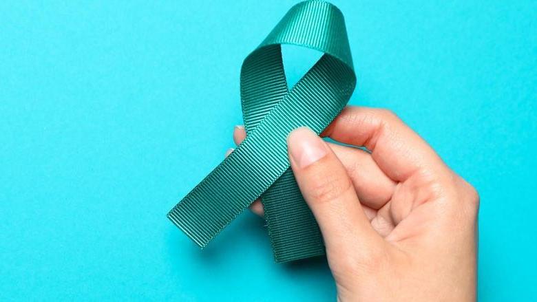 Woman holding teal awareness ribbon on light blue background, top view with space for text. Symbol of social and medical issues